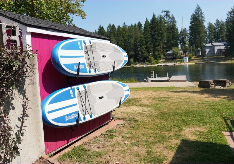 Paddleboards stored against a bright pink shed wall beside the lake