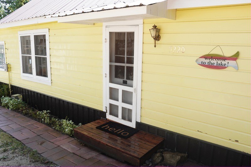 The pale yellow cabin, its white screen door, the number 5220 and a painted fish sign reading welcome to the lake